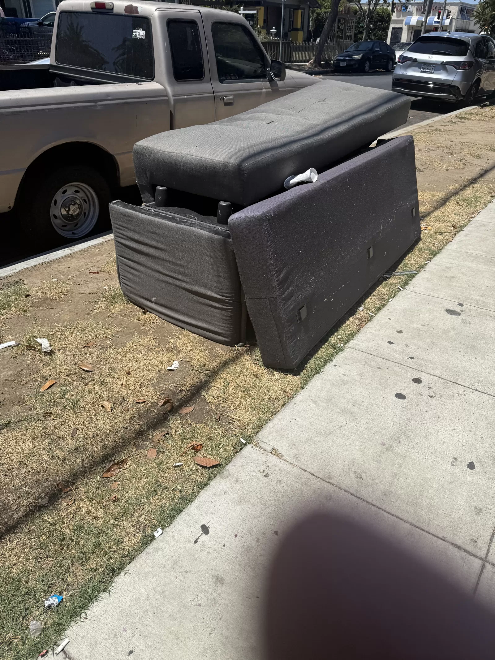 Multiple large black upholstered furniture sections are stacked on the grass strip next to the sidewalk.